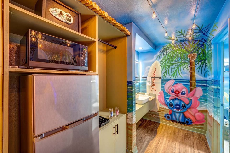 Kitchenette area with a microwave, mini fridge, and a colorful beach-themed mural featuring cartoon characters.
