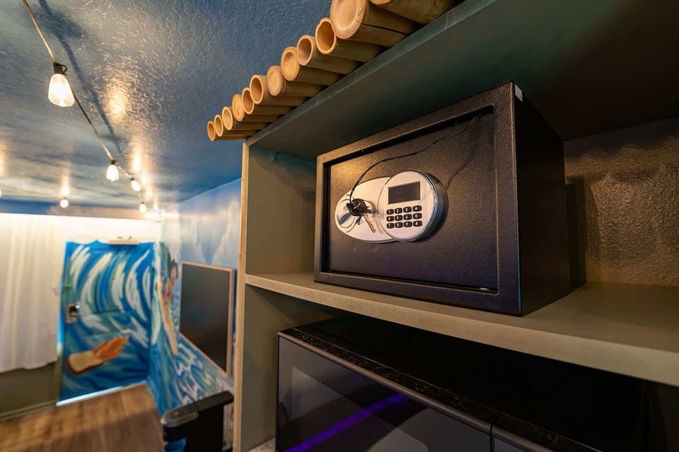 A secure electronic safe is conveniently located on a shelf in the room with artistic wall murals and string lighting.