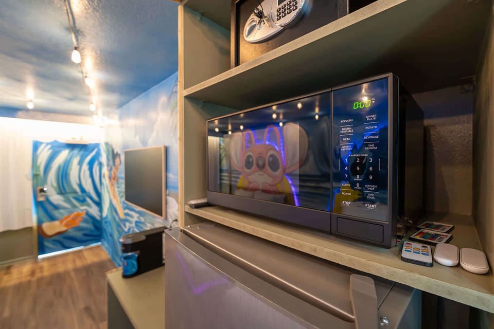 Compact kitchen area featuring a microwave and mini fridge with colorful wall art in the background.
