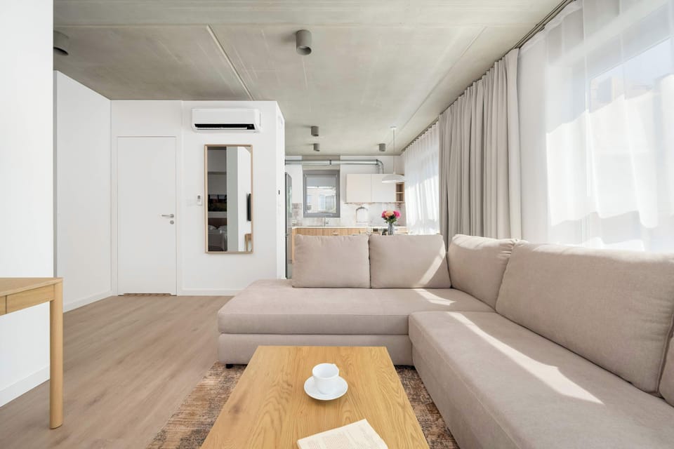 A bright living room with a comfortable sofa bed and a dining table for six. Large windows fill the space with natural light.