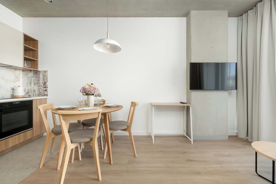 A bright living room with a wall-mounted TV and a dining table for four. The open layout creates a spacious and inviting feel.