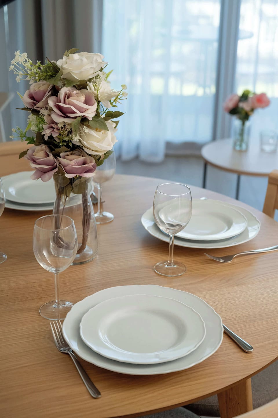 A close-up of a dining table with neatly arranged plates and cutlery. The setting invites guests to enjoy a shared meal