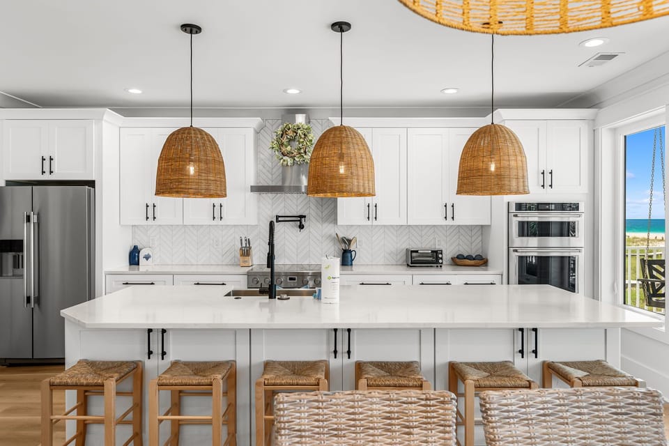Your gourmet kitchen awaits with pristine white countertops, woven pendant lights, and stunning ocean views through the window.