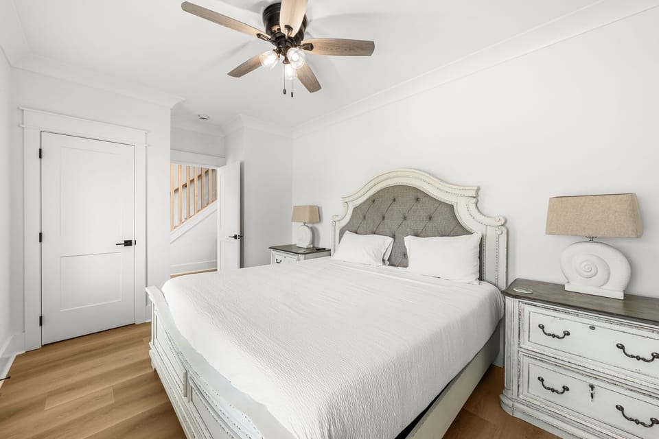 Drift off to sleep in your elegant bedroom, featuring a luxurious tufted headboard, crisp linens, and gentle ceiling fan for perfect comfort.