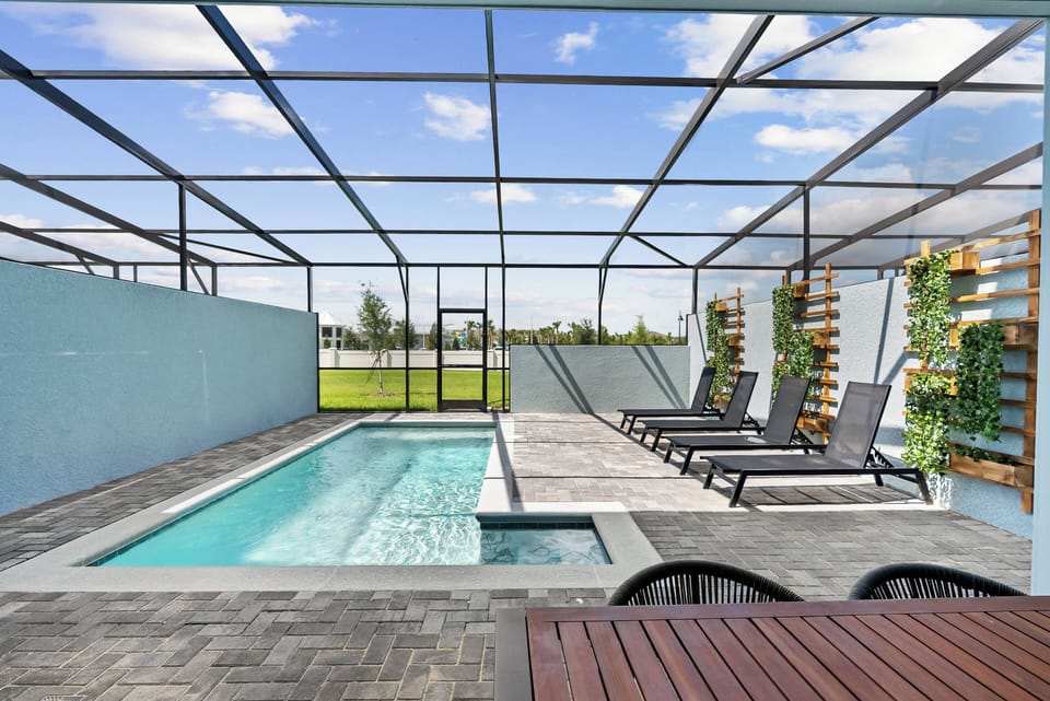 Discover your private oasis featuring a shimmering pool and stylish loungers for ultimate relaxation. The modern screened enclosure allows for refreshing breezes while highlighting beautiful greenery beneath the clear blue sky.