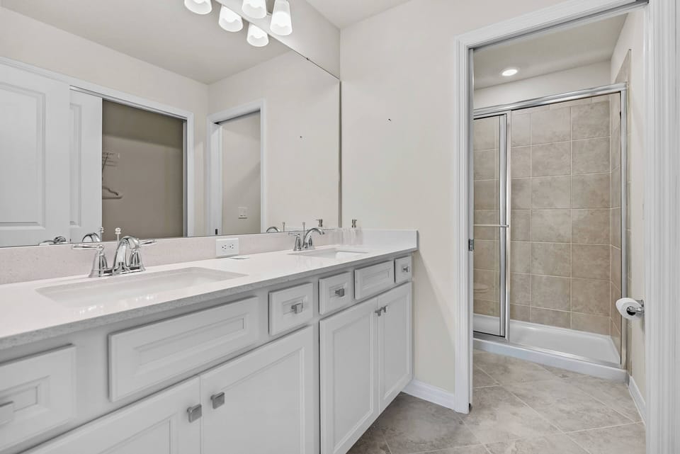 Experience a bright and spacious bathroom with a double vanity and sleek white cabinetry. Warm neutral tones and an elegant tile shower create a clean, refreshing atmosphere for your stay.