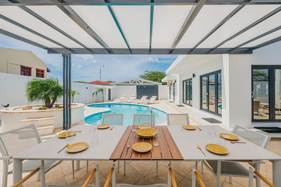 Sunny resort pool deck with sleek gray loungers, rolled white towels, and a glimmering blue pool.