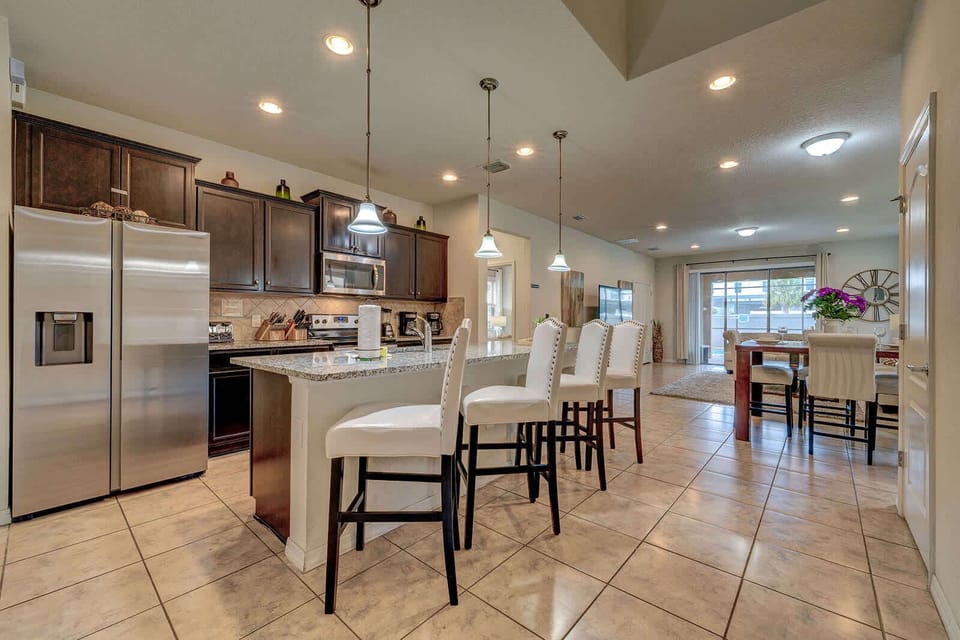 Modern kitchen with granite island and seating for four overlooking the dining and living area.