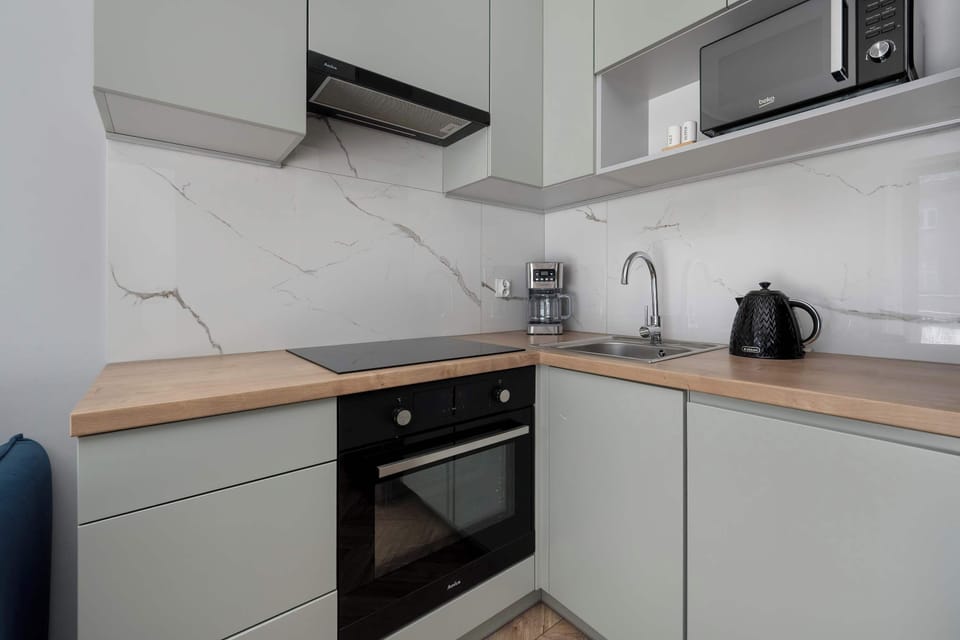 Modern kitchen with white cabinets, wooden countertop, and practical appliances including oven, fridge, kettle, and coffee machine.