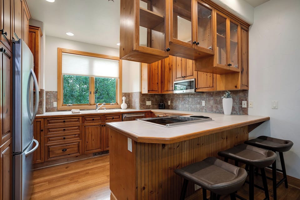Your fully equipped kitchen features rich wood cabinetry, modern appliances, and a breakfast bar where you can enjoy morning coffee with garden views.