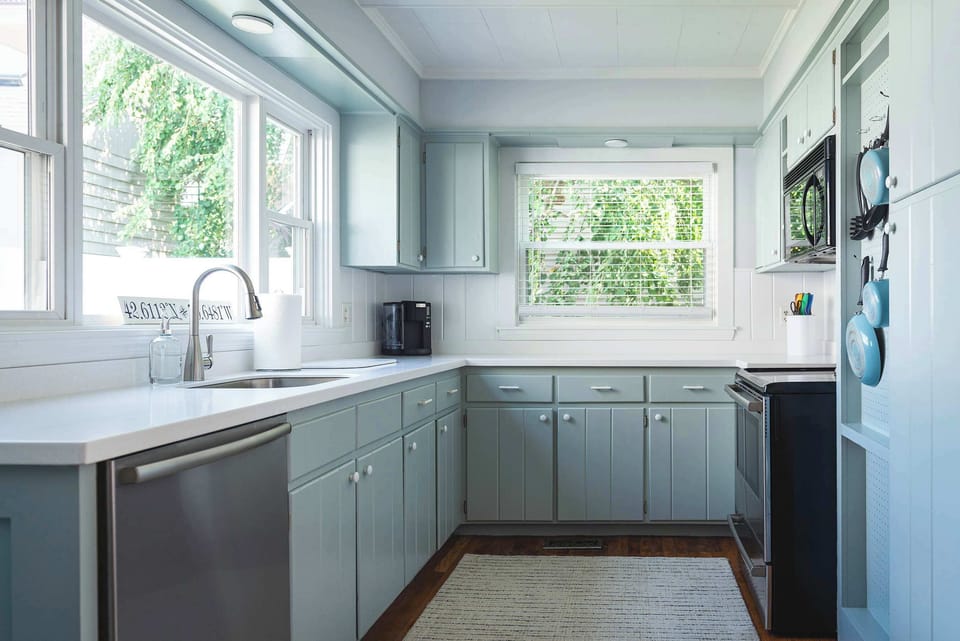 Light-filled kitchen with sage cabinetry and stainless appliances