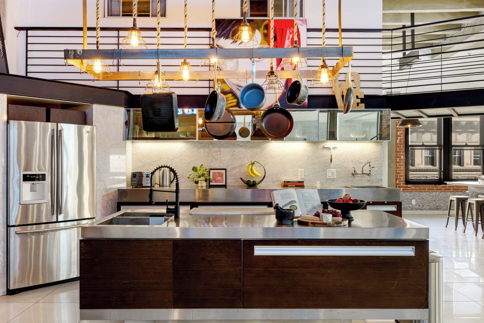 A sleek, industrial-style kitchen with stainless steel appliances, a central island, and unique pop-art wall decor.