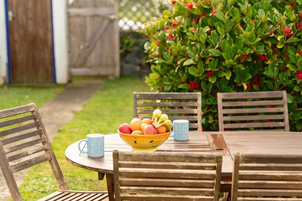 Patio table and chairs with a bowl of fruit. Small lawn and path to rear gate