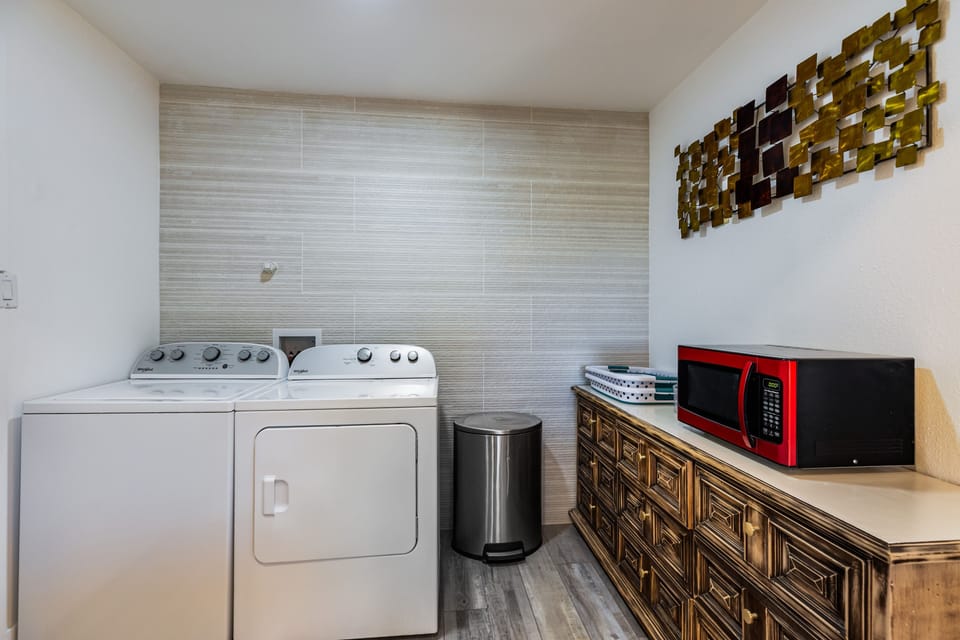 Laundry area with a washer, dryer, and an ornate cabinet holding a red microwave.