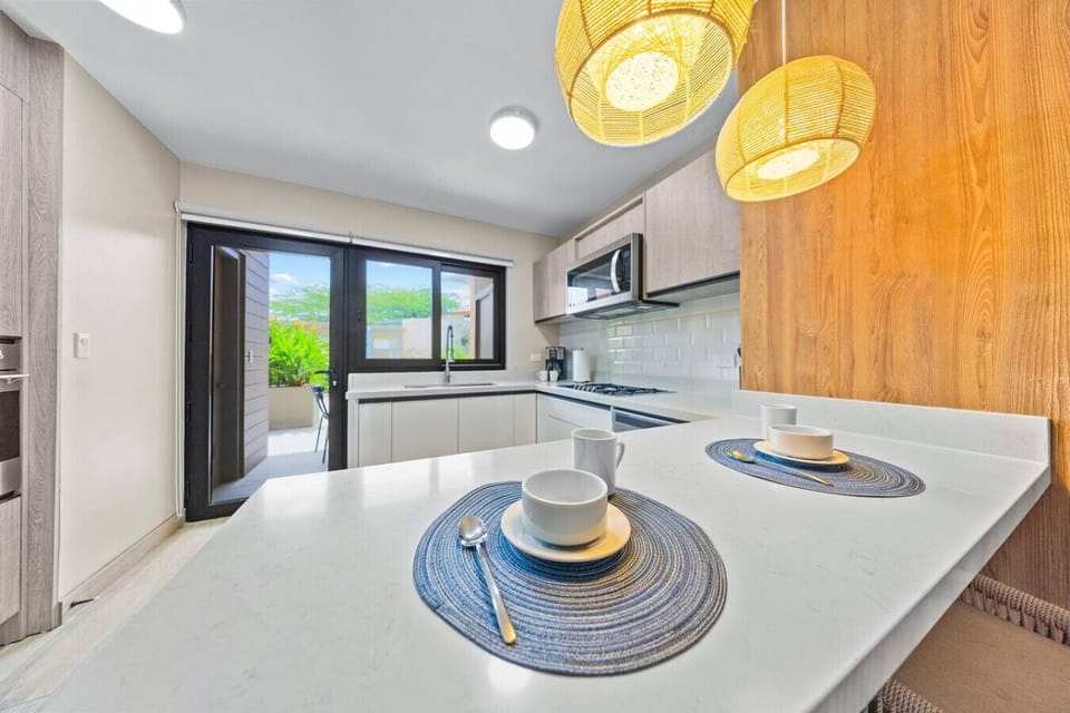 bright kitchen featuring modern appliances, a white countertop, and pendant lighting over the breakfast bar. A sliding door offers a view of a landscaped area.