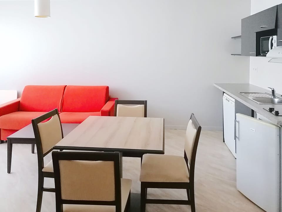 Bright living and dining area featuring a red sofa and dining table with direct access to the kitchen.