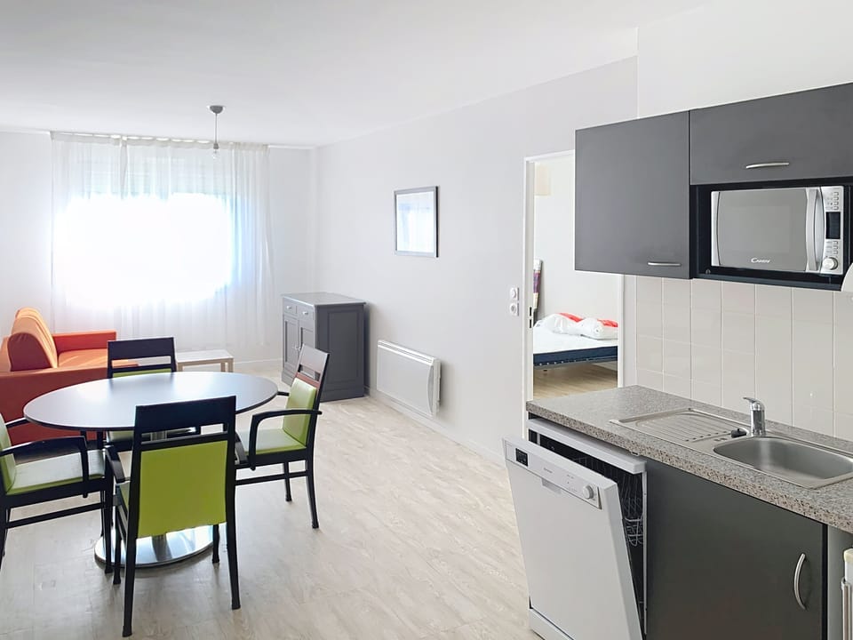 Open plan kitchen and living area with dining table and green accent chairs.