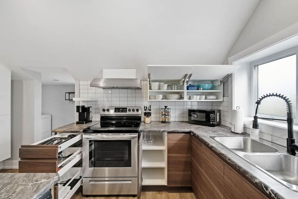 A full modern kitchen featuring stainless steel appliances: oven, stovetop, microwave, and refrigerator. Dark granite counters, a double sink, and ample cabinet space. Includes a coffee maker and cooking essentials for your convenience.