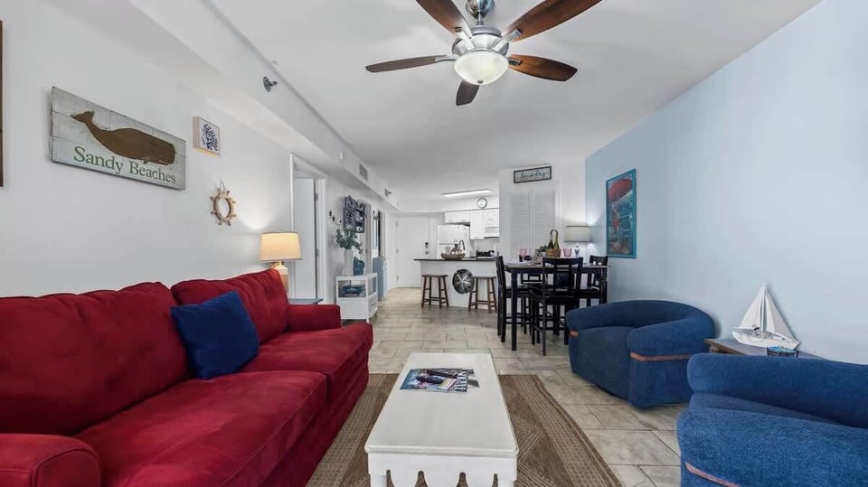 {LIVING ROOM} Relax in the cozy living room with a plush sofa, warm lighting, and easy balcony access. Perfect for crisp fall evenings sip cocoa, watch a movie, or step outside to enjoy the ocean breeze.