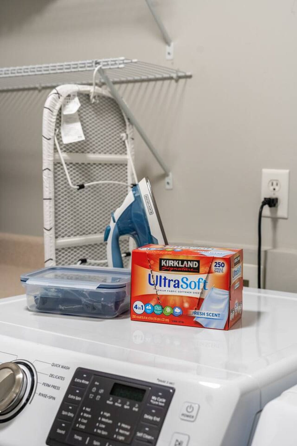Laundry area detail with full‑size washer, wall shelving, iron and ironing board.