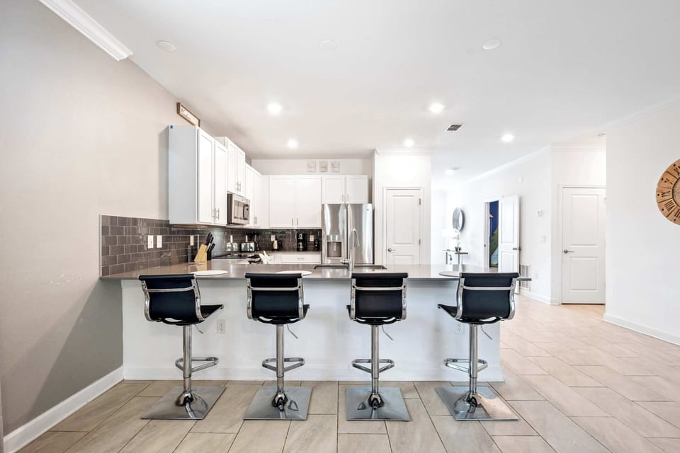 Contemporary kitchen with white cabinets, dark tile, and bar seating.