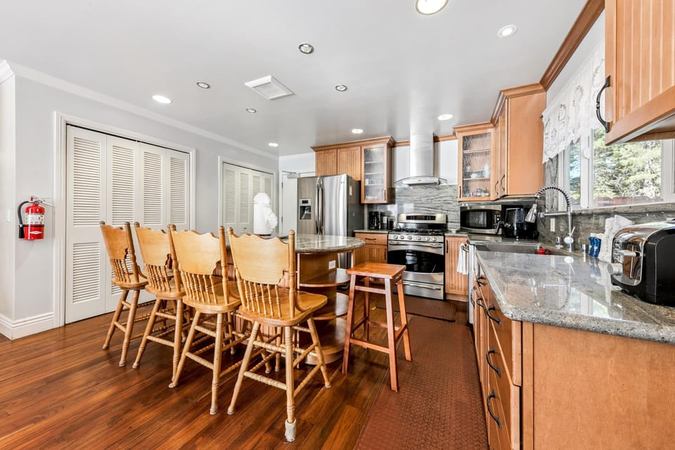 Dining island with six spindle-back wooden chairs sits on polished hardwood floors beside granite countertops.