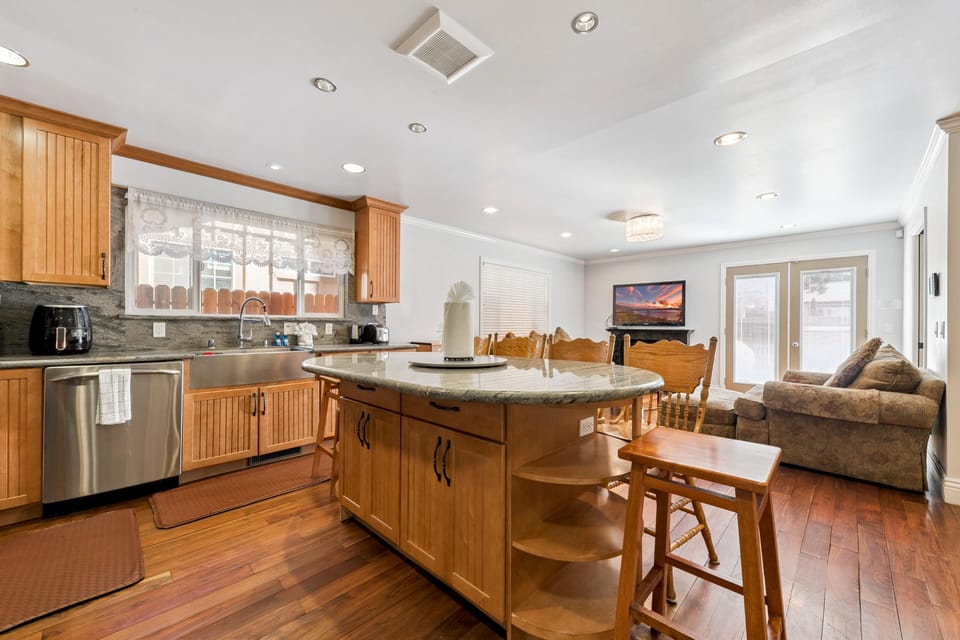 Kitchen island with granite countertop and wood stools faces hardwood floors and a dining area with carved wooden chairs.