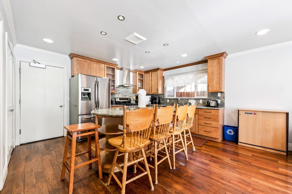Wood-paneled kitchen with granite island, stainless steel appliances, and five spindle-back wooden stools.