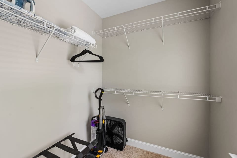 Main bedroom closet with hangers, iron, ironing board, fan, and vacuum