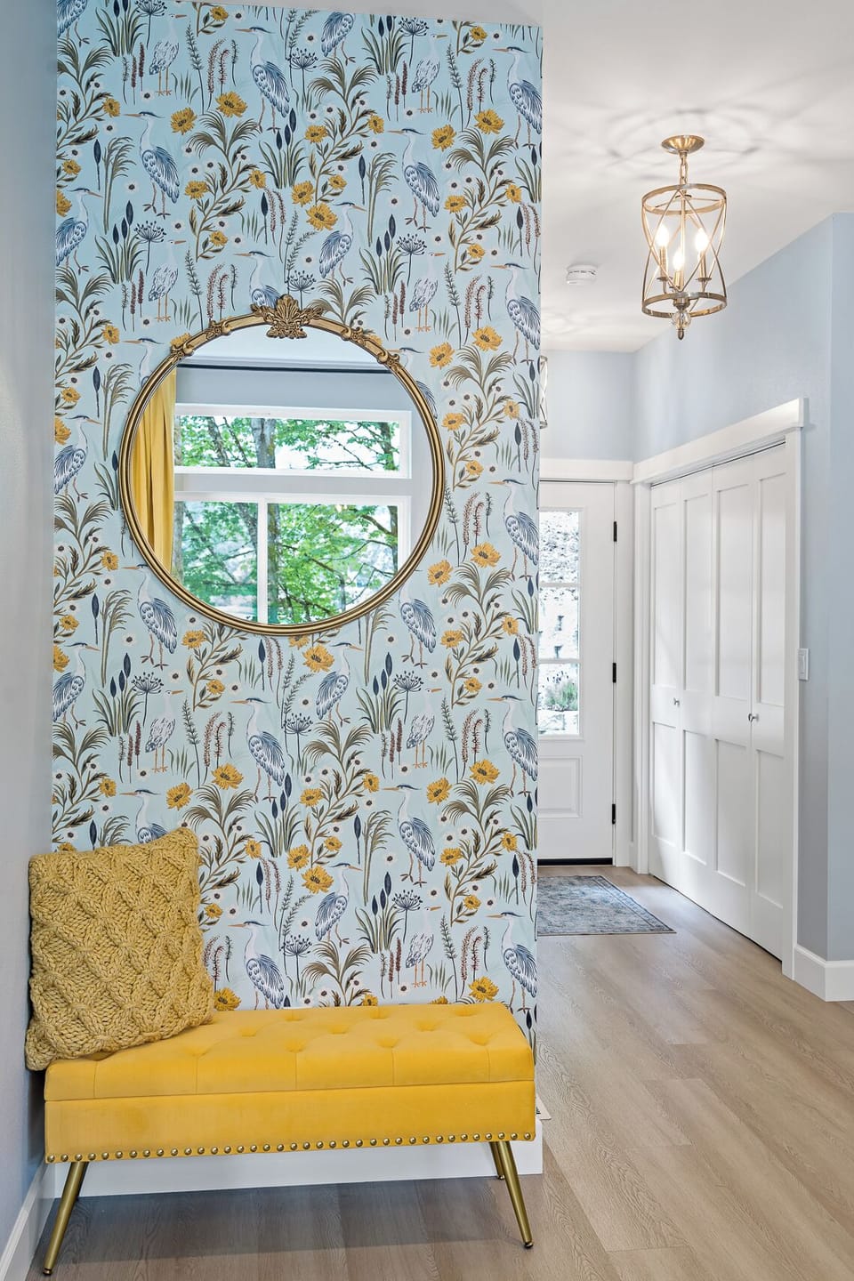 Bright, stylish entryway with floral wallpaper, gold mirror, and chic bench