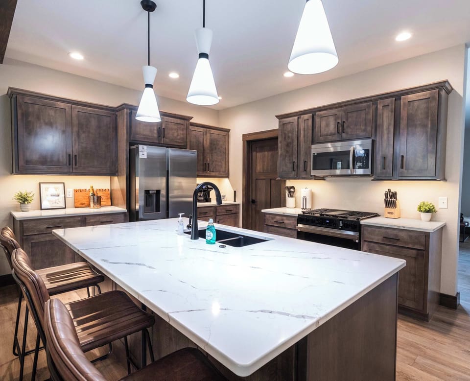 Modern kitchen with sleek quartz counters, stainless-steel appliances, and warm wood cabinetry. The large island with bar seating is perfect for morning coffee or gathering while meals are prepared.
