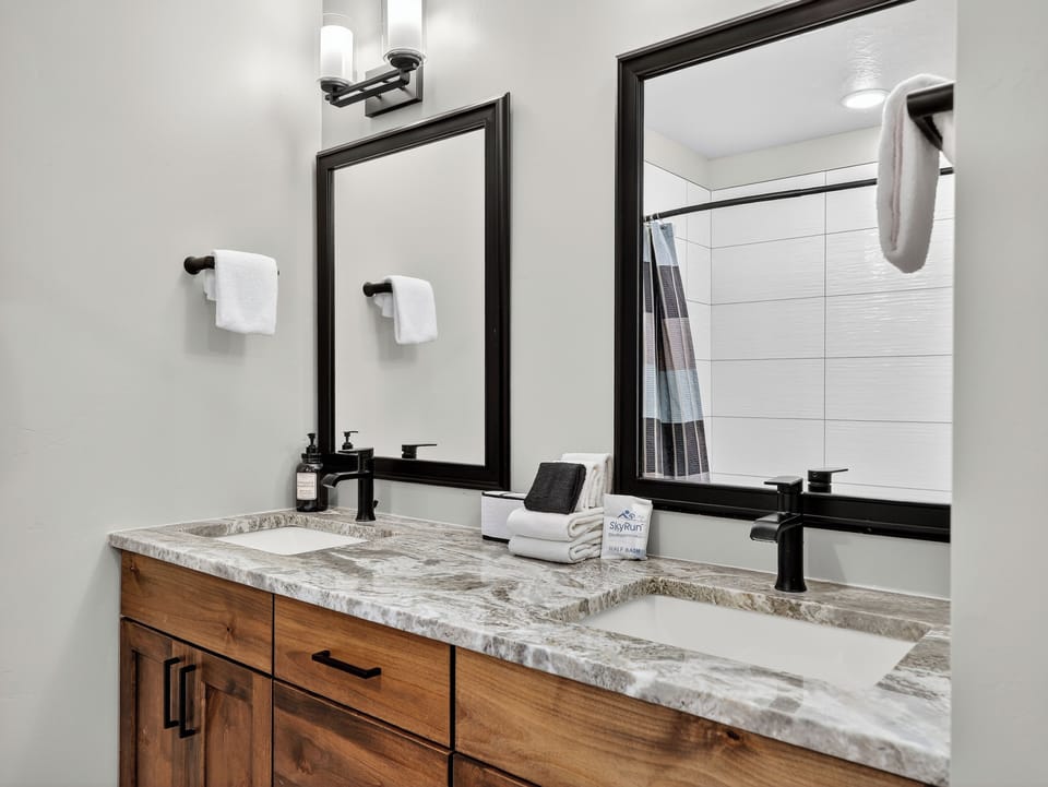 Primary bathroom featuring double-sink vanities, custom cabinetry, and a shower/tub combo