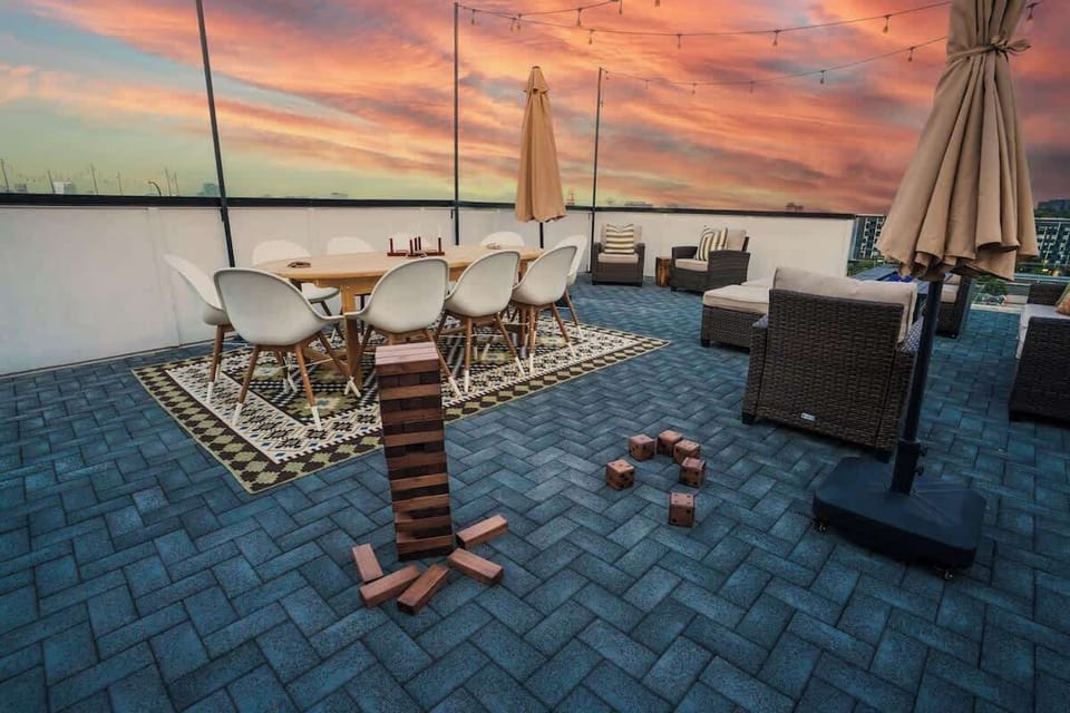 Rooftop deck at sunset with wooden lounge chairs, an umbrella, and blue tile flooring