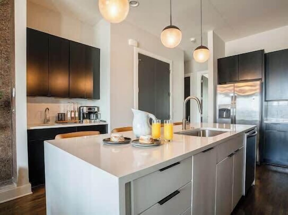 White kitchen with a large island, pendant lighting, and stainless steel appliances