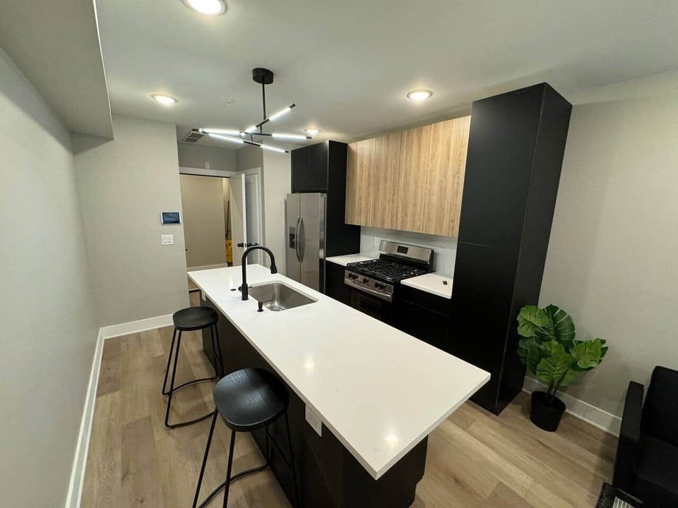 The kitchen counters have been elegantly designed in a sleek black finish. features a large quartz island with barstools. Equipped with appliances, including an oven stove, hood, refrigerator, microwave, dishwasher, and garbage disposal.