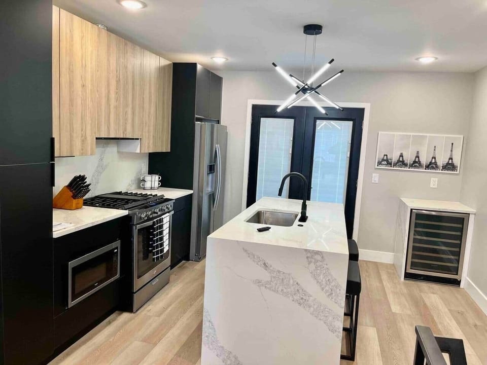 This kitchen features a waterfall quartz island, a professional oven, hood,a 36-inch refrigerator, a dishwasher, a wine cooler, a microwave, and a Keurig coffee maker. 