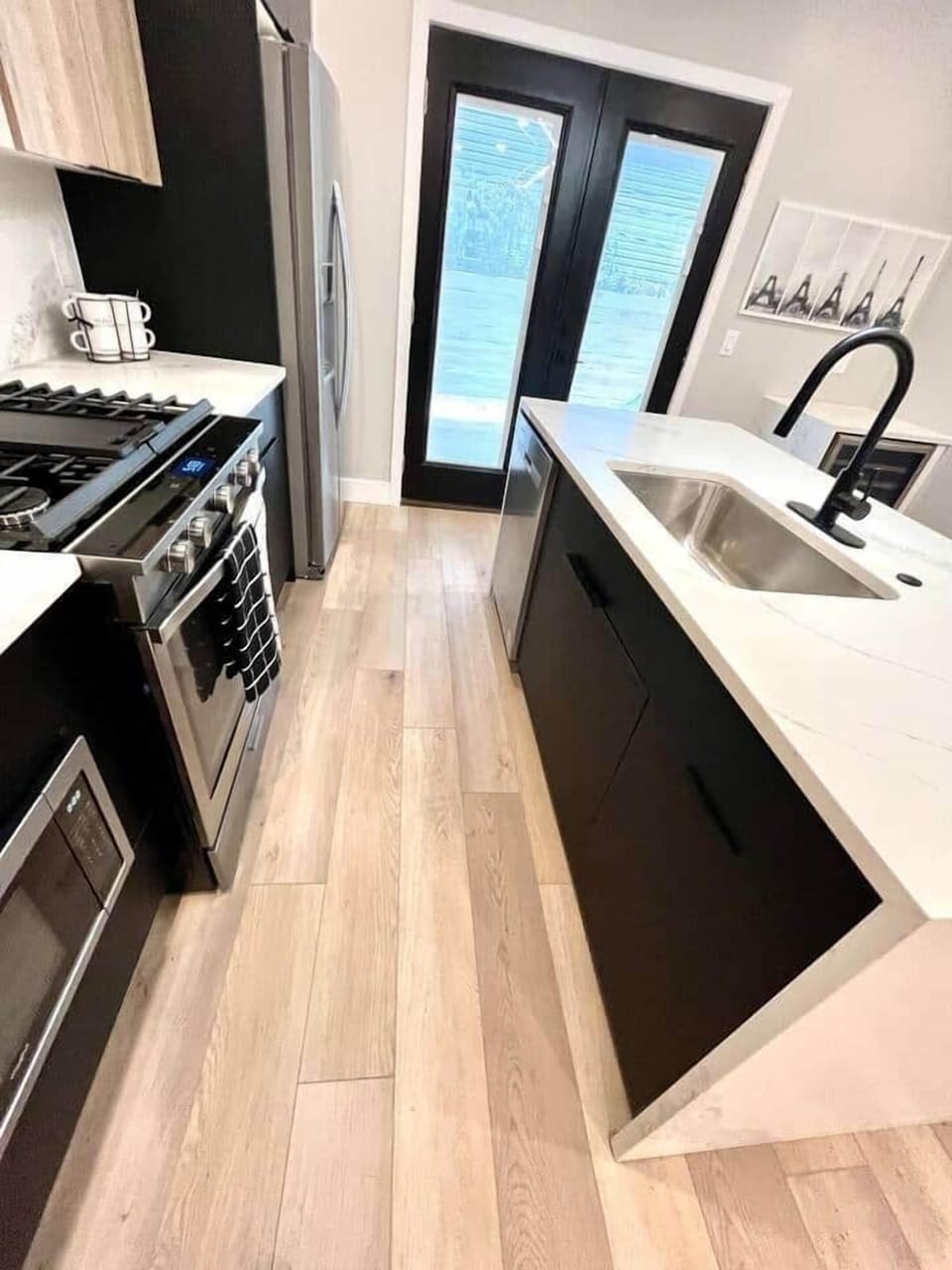 This kitchen features a waterfall quartz island, a professional oven, hood,a 36-inch refrigerator, a dishwasher, a wine cooler, a microwave, and a Keurig coffee maker. 