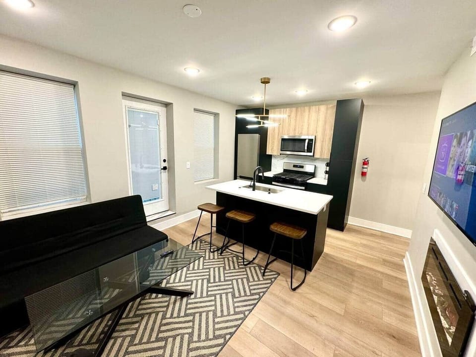 The kitchen is equipped with a sophisticated quartz countertop island, complete with sleek barstools. It seamlessly connects to the inviting living room, which features a large flatscreen TV and a cozy fireplace.