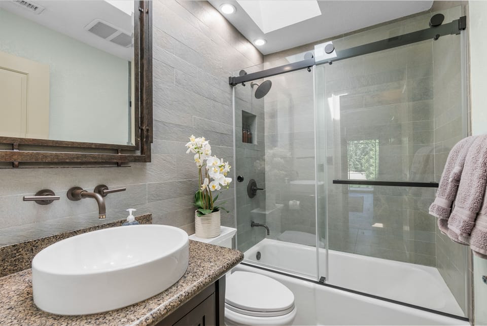 Contemporary bathroom featuring a vessel sink vanity and glass-enclosed shower-tub combination.