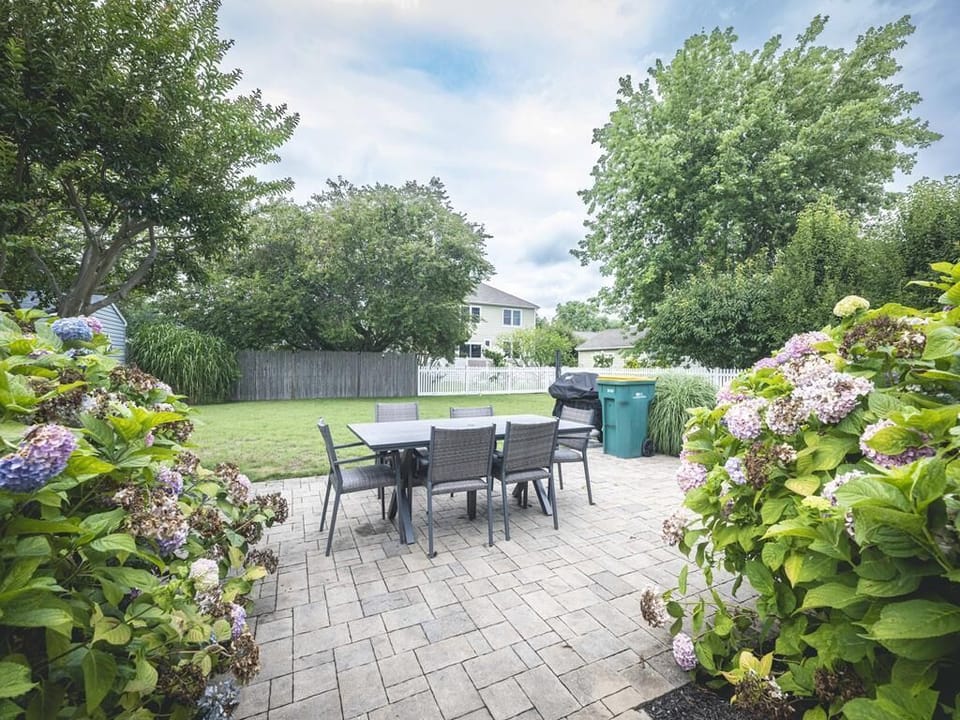 The outdoor dining in the spacious backyard, surrounded by lush greenery and vibrant hydrangeas, is perfect for family gatherings and summer barbecues.