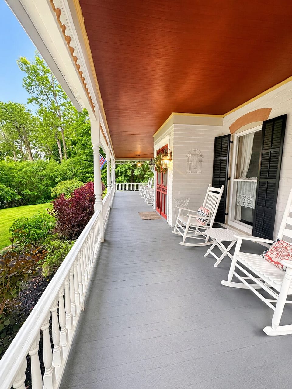 Covered wraparound porch with rocking chairs and shaded seating.