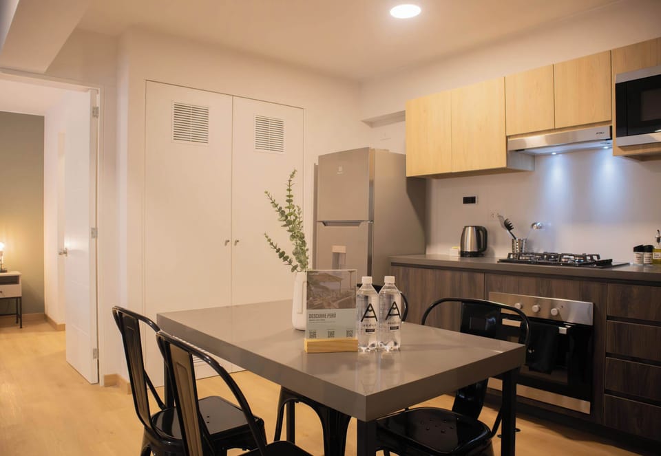 A modern kitchen with light wood cabinetry, black countertops, and stainless steel appliances.