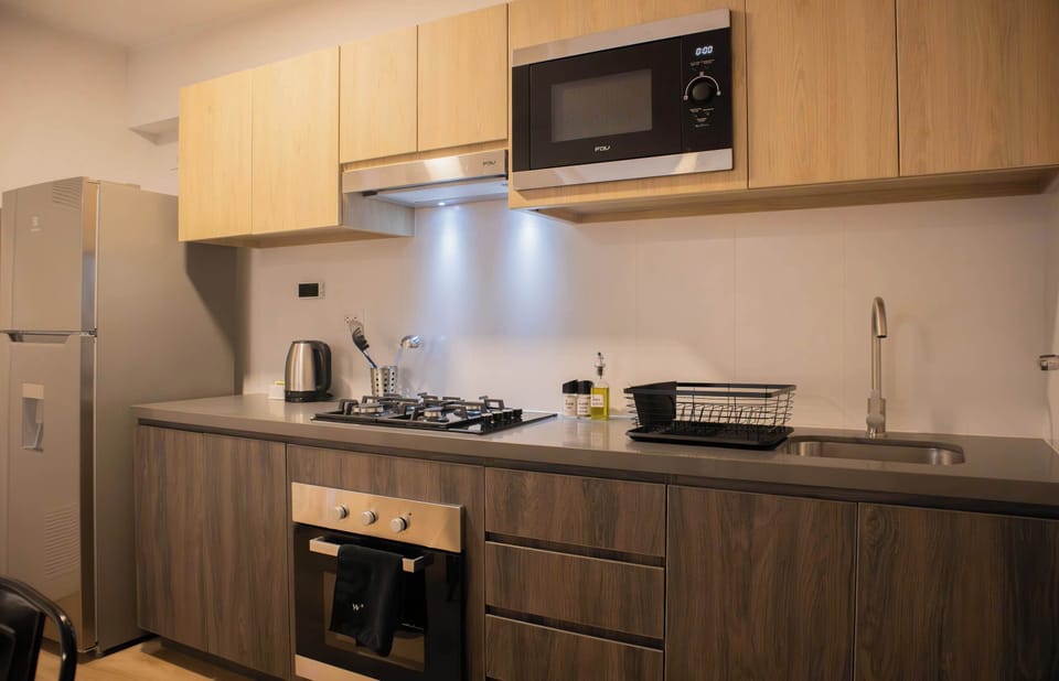 Compact kitchen with microwave, stove, and kettle.