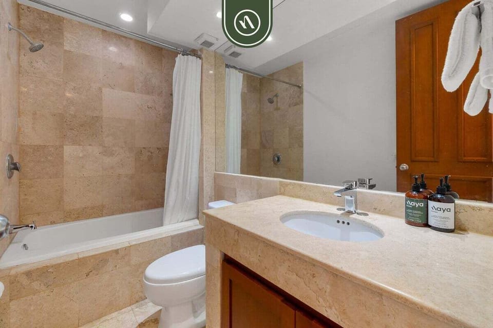 This full bathroom offers a clean aesthetic with natural stone tiling, a large bathtub with a shower combo, and ample counter space for your essentials.