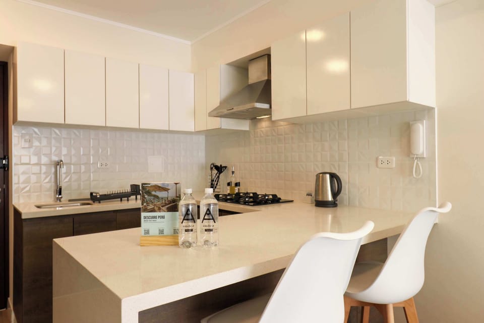Open kitchen with a bar counter, white cabinets, and two white barstools.