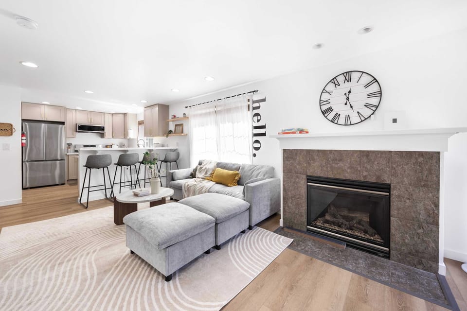 Bright & Airy Open-Plan Living----Cozy gray sofa with mustard accents, round coffee table, and layered rugs. 