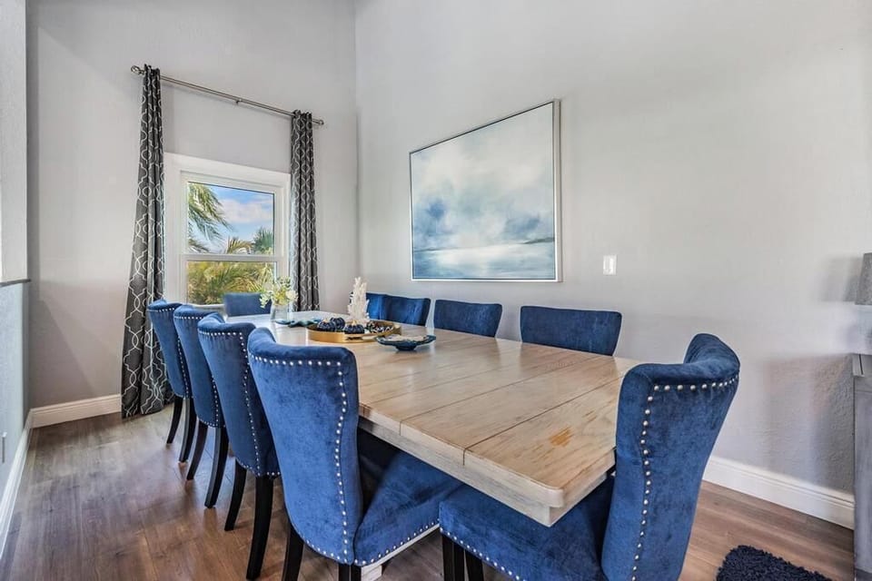 Sophisticated dining room with a polished wooden table, luxe navy velvet chairs, and chic coastal décor. Bathed in natural light, it’s the perfect space to gather for family meals, celebrations, or elegant dinner parties.