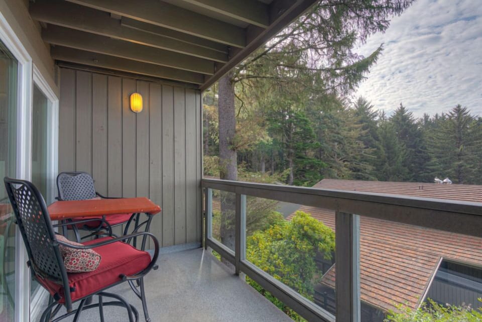 The forest-view patio invites you to unwind with a small table and chairs, surrounded by serene greenery for a peaceful retreat.