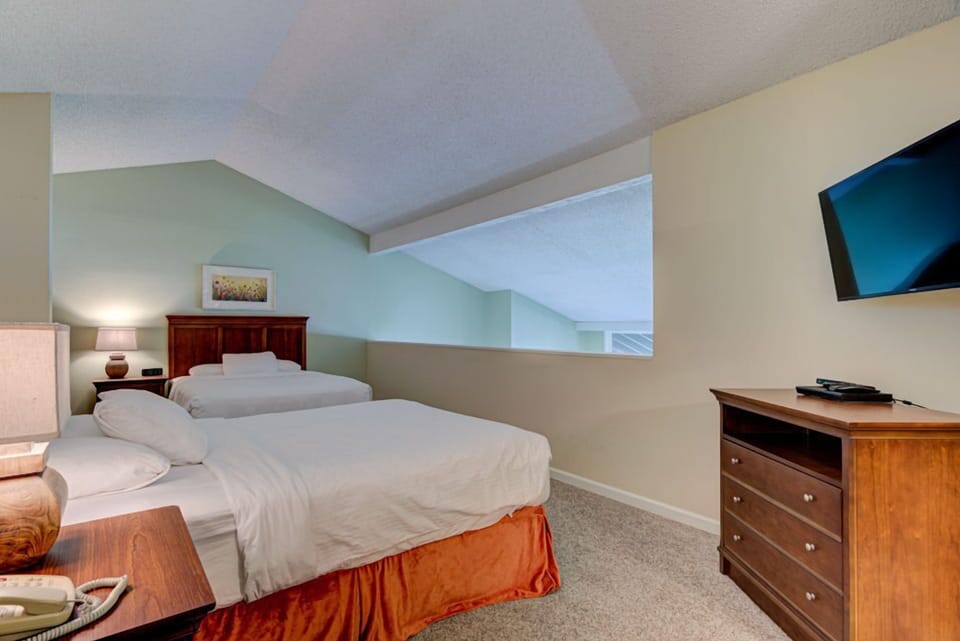The upper level of the loft provides an inviting atmosphere with additional sleeping space, highlighted by its light-filled design and cozy furnishings.