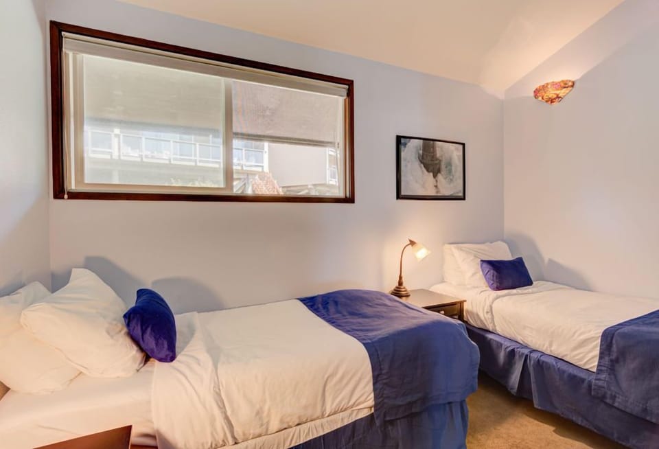 Cozy and inviting, this bedroom features two twin beds adorned with stylish blue linens and a large window inviting natural light, perfect for restful nights.